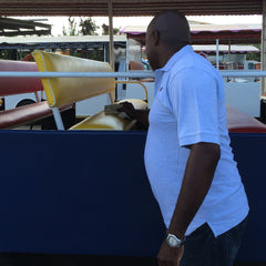 Man in a light blue polo shirt inspecting a small, open-air vehicle with yellow and red seats.